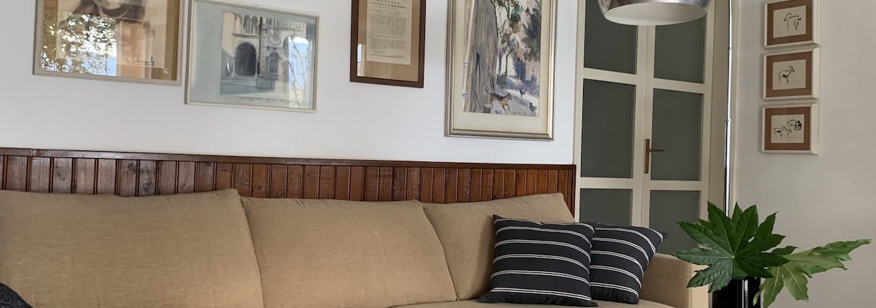 Nel living di questa casa degli anni 60’ domina alle pareti una bella boiserie in legno. Tra i molti quadri della padrona di casa è stata individuata una selezione declinata sugli azzurri suggerita dal tappeto a righe in lana. L’effetto voluto rinnova lo spazio dedicato al relax davanti al lago, mixando mobili anni 80’, vintage e piccoli tavoli etnici.